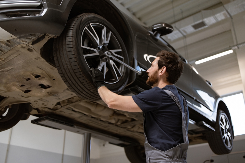 Mechanic in auto repair shop adjusting car tire on lift using professional tools. Image depicts vehicle maintenance, tire service, and automotive expertise.