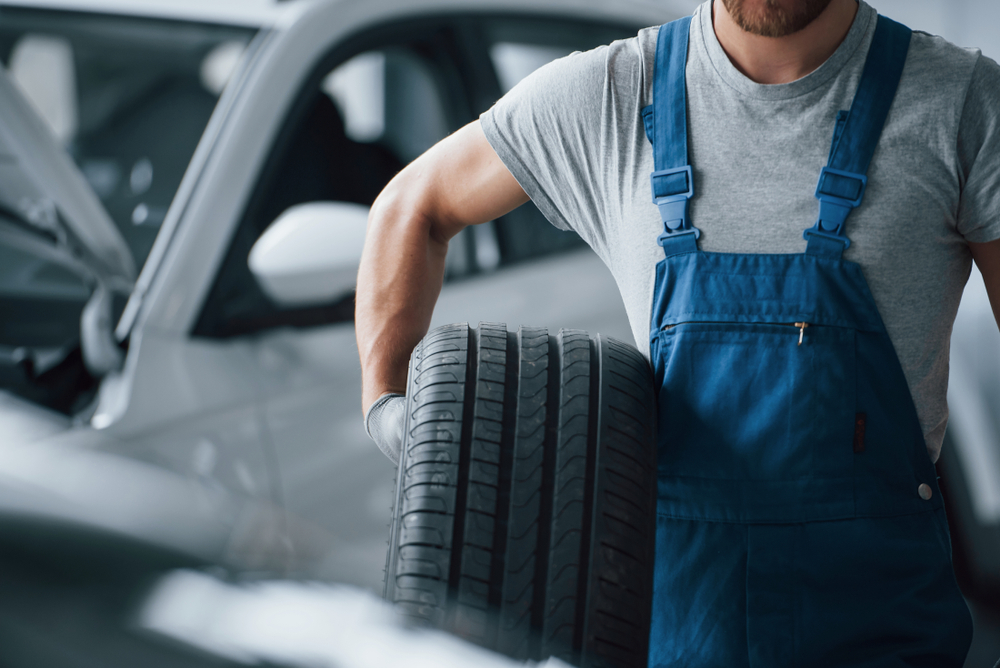 Unshaved man. Mechanic holding a tire at the repair garage. Replacement of winter and summer tires.